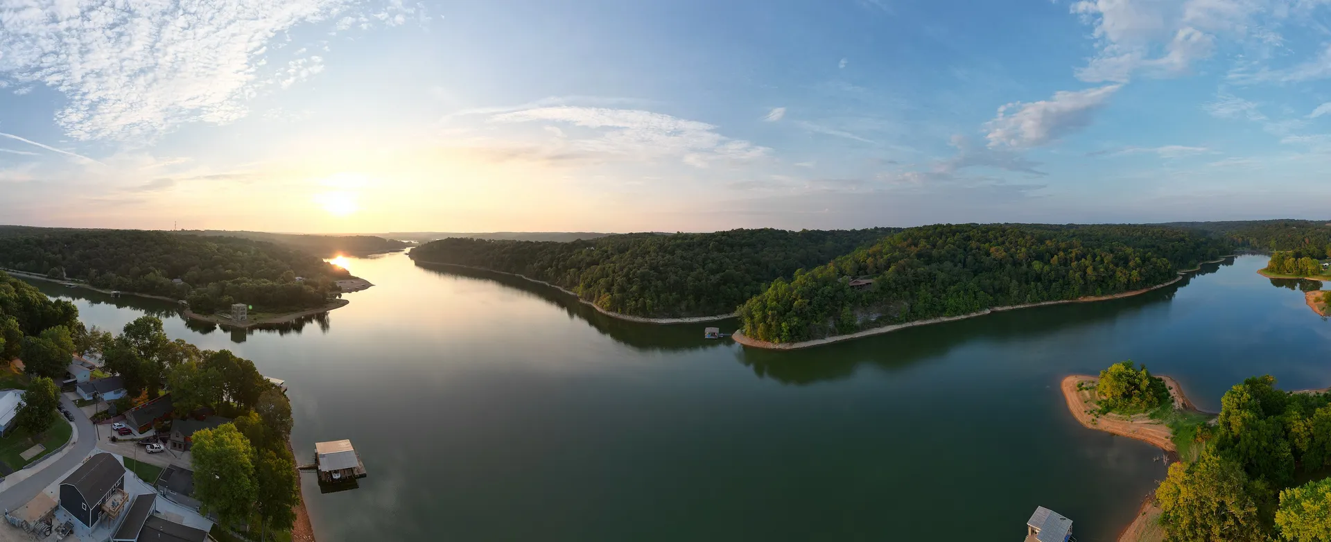 Panoramic drone view along a wooded Beaver Lake shoreline, boat docks and a cove in low morning light