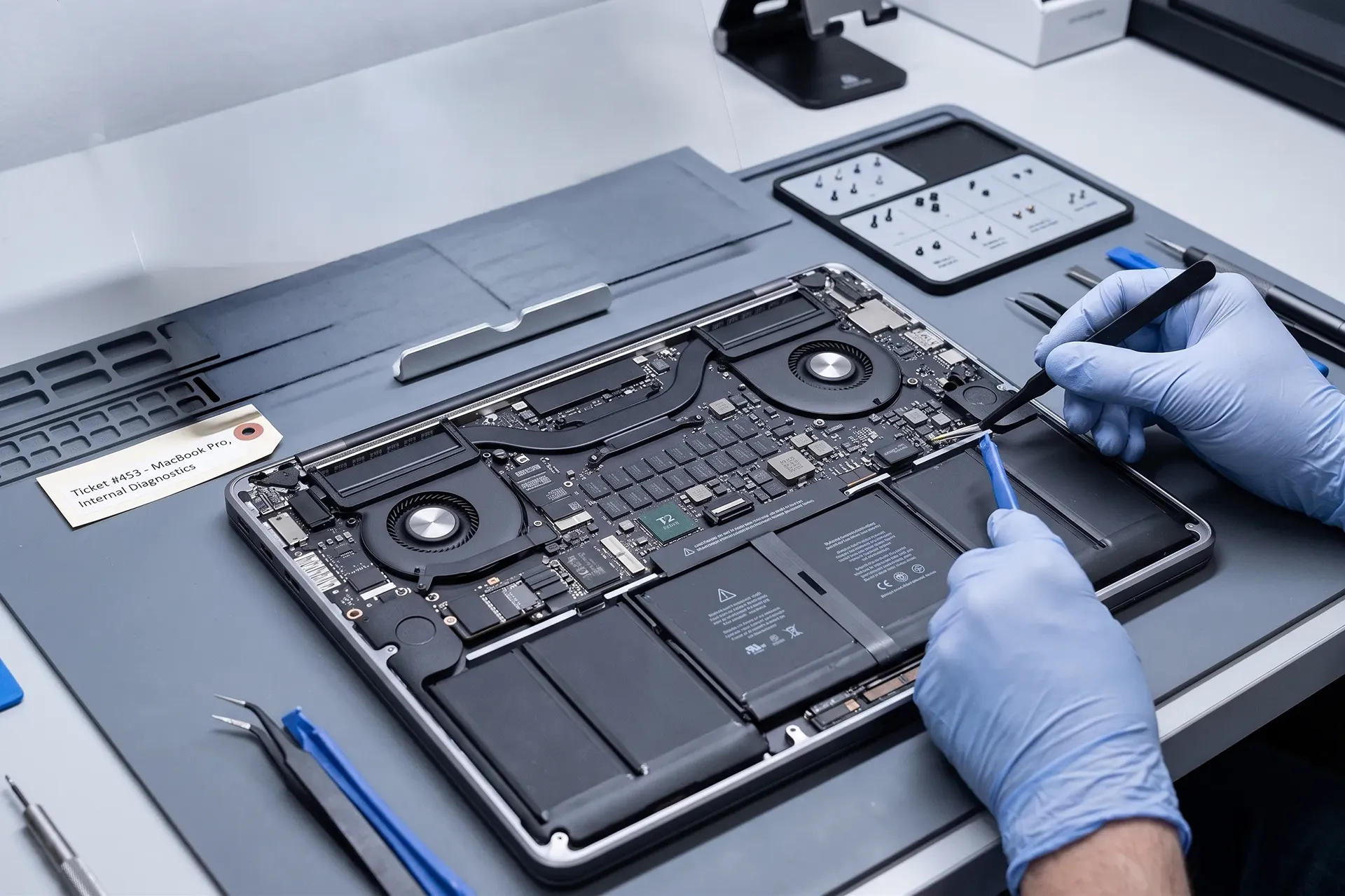 A MacBook Pro opened on a repair bench with the back cover off, showing the battery cells, fans and logic board